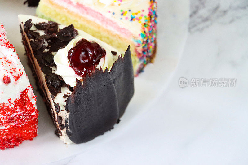 近距离图像的蛋糕品种切片在圆形的防油羊皮纸，黑色森林蛋糕，彩虹蛋糕，红色天鹅绒，大理石效果的背景，高架视图，重点在前景，复制空间
