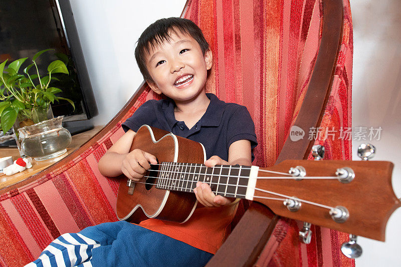 小男孩坐在红沙发上弹吉他