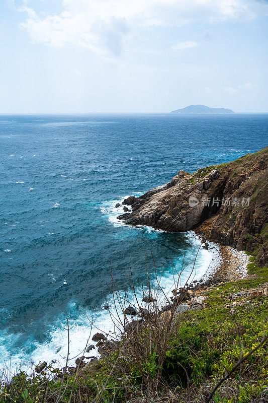 海浪拍打着海滩上的岩石，海水随着阳光飞溅到天空。一个宁静的越南孔岛，是越南海岛的天堂