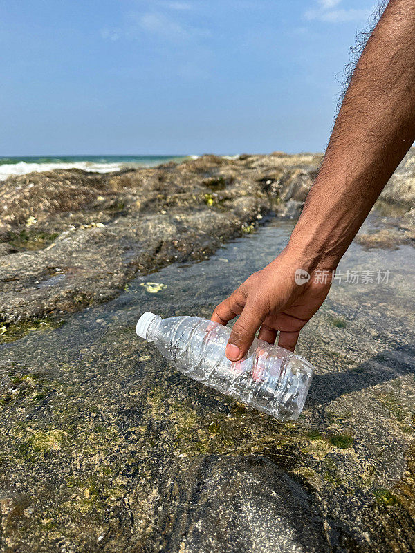 图片:在退潮时，白色盖子的透明塑料水瓶被冲走在岩石池中，被不认识的人捡起，海岸上的海洋垃圾和污染，乱扔的沙子，肮脏的海滩，重点在前景