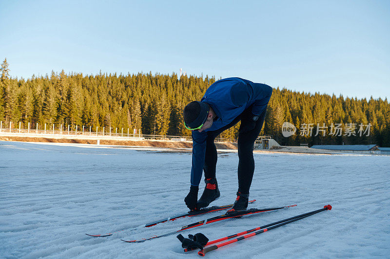 帅气的男性运动员与越野滑雪板准备装备训练在雪林。检查smartwatch。健康的冬季生活方式。