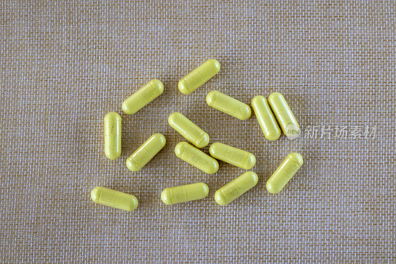 黄色的槲皮素胶囊，米色的自然纹理背景。膳食补充剂俯视图。它是一种类黄酮，对过敏、哮喘有抗组胺和抗炎作用。