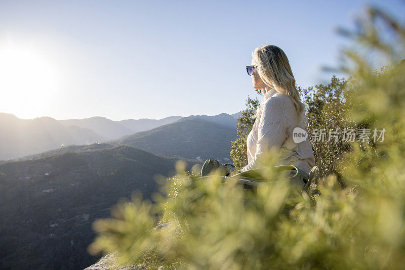 成熟的女徒步旅行者在远山的山顶上放松