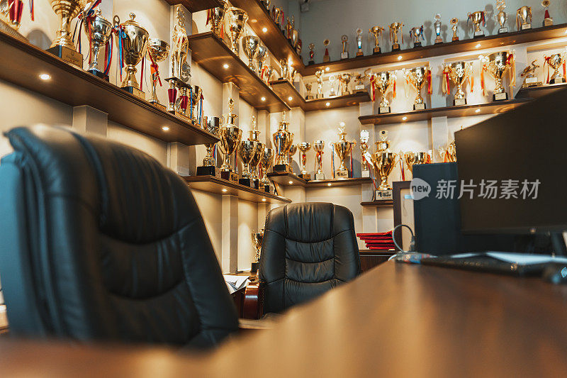 一个办公空间和桌子，背景的架子装饰着多年来赢得的冠军奖杯