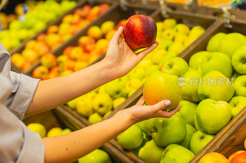 年轻的金发女郎在水果区挑选苹果。秋季市场。素食主义。健康食品。选择。购物