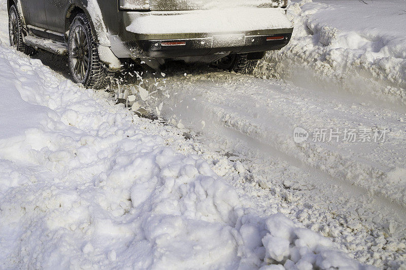 路上的雪从汽车的转轮上飞了起来。汽车的车轮旋转并喷出雪块，它试图在湿滑的道路上获得牵引力。
