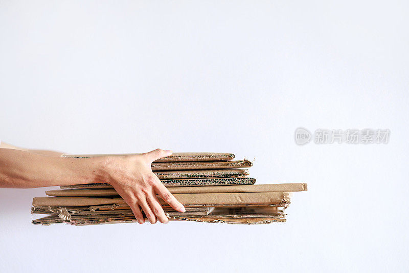 一名亚洲妇女拿着一堆折叠的纸板，准备回收，展示了一种可持续的生活方式
