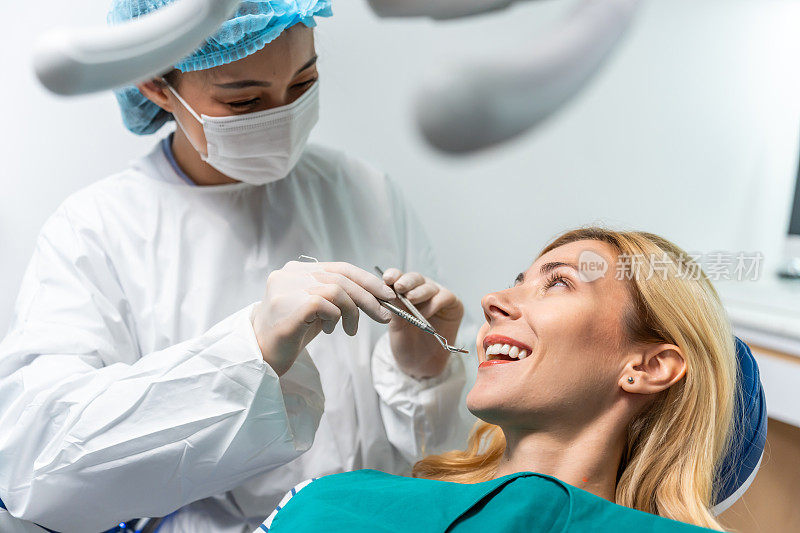 女牙医在牙科诊所为白人女孩检查牙齿。美女病人躺在牙科椅上，在医院的牙科预约服务中接受医生的牙科治疗