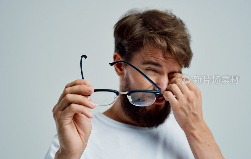 一个眯着眼睛的男人手里拿着眼镜，背景很浅，视力有问题