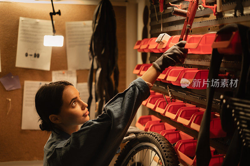 一个女机械师在车库的墙上挂一个活动扳手的特写。自行车维修及保养