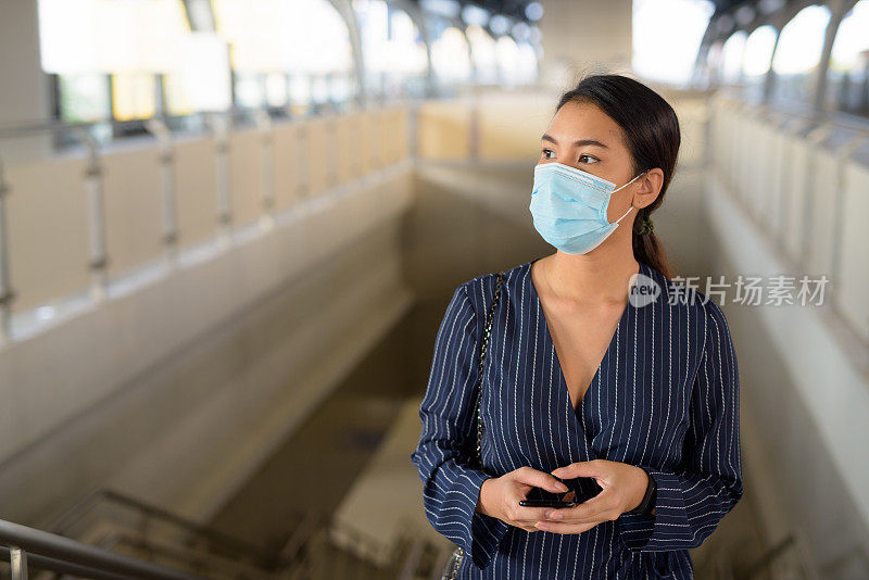 年轻的亚洲女商人戴着面具在轻轨站上思考