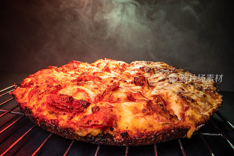 广角拍摄的美味热气腾腾的深盘皮辣香肠披萨新鲜出炉的烤箱在冷却架下的加热灯与复制空间