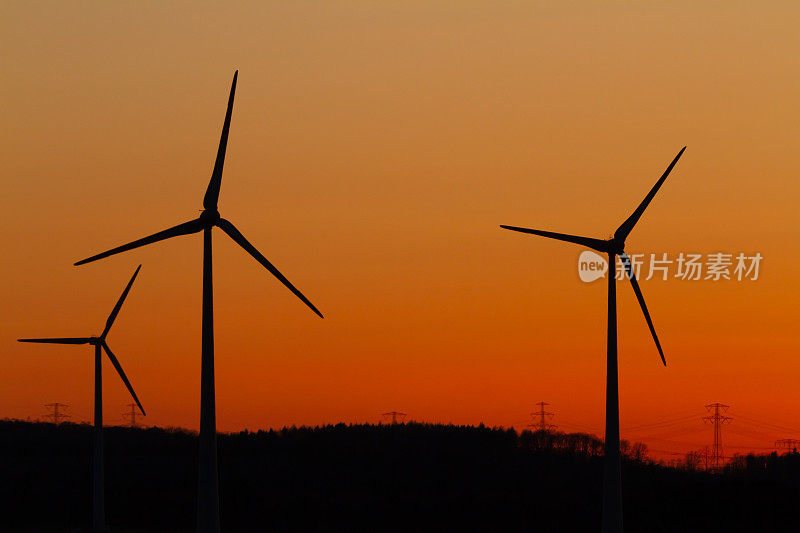日落时一组风力涡轮机塔的剪影