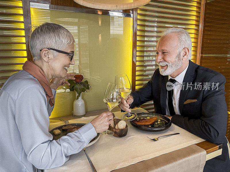一对老年夫妇在一家高档餐厅享用午餐时用气泡酒敬酒