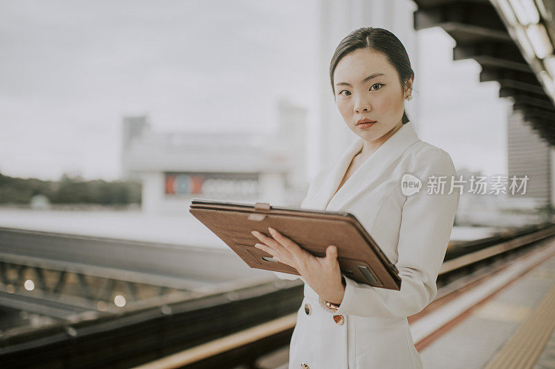 一位年轻的亚洲华裔女商人带着她的数字平板电脑在单轨火车站等待火车