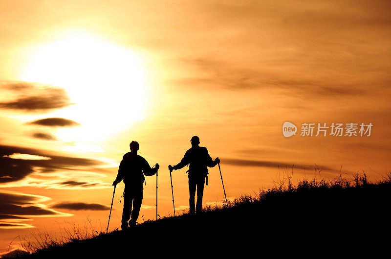 两个年轻的徒步旅行者的剪影与背包和波兰人欣赏美丽的日落