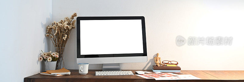 一个木制的工作空间被一个白色的空白屏幕电脑显示器和各种设备包围着。