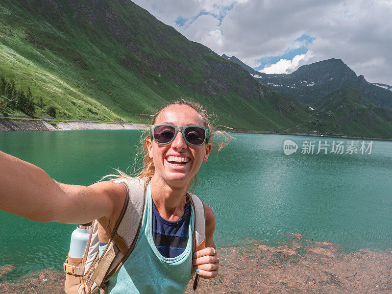 年轻女子在美丽的高山湖周围徒步旅行时自拍