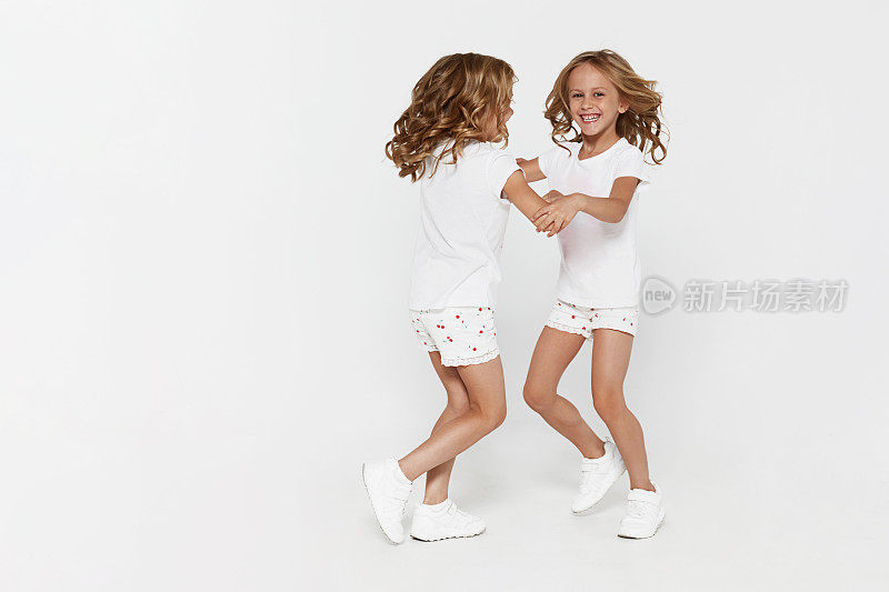 微笑有趣的小双胞胎姐妹在白色的衣服跳舞孤立在白色的背景儿童工作室肖像。