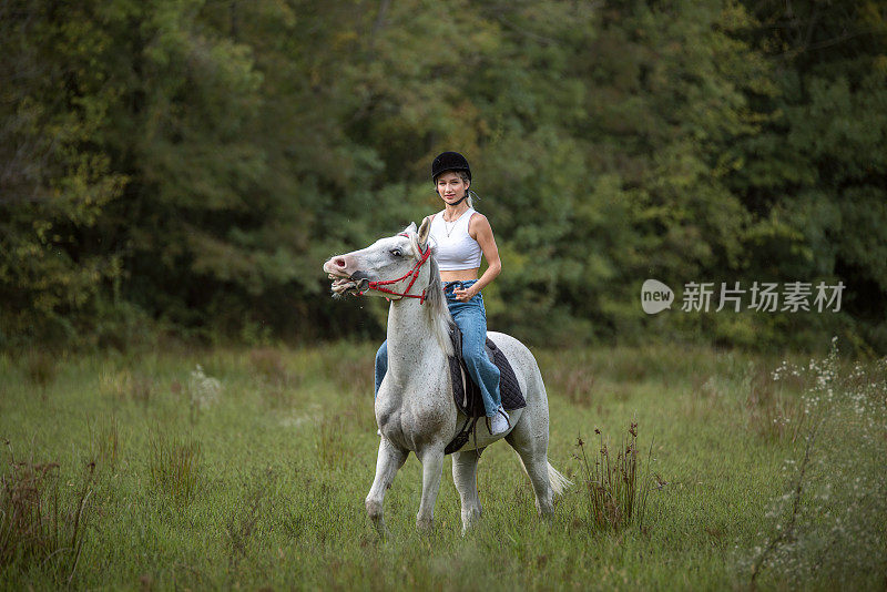 年轻美丽的女人和她的马在牧场自由漫步