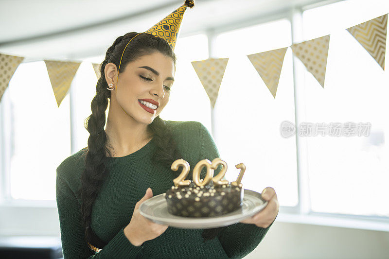 一名年轻女子在家庆祝圣诞节，手里拿着巧克力蛋糕，蛋糕上插着2021年的蜡烛