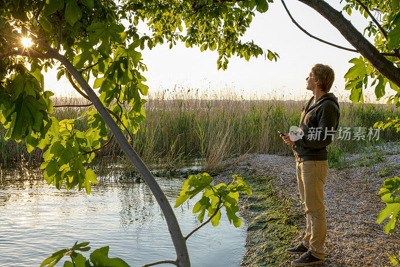 日落时分，一名年轻人在湖边使用手机