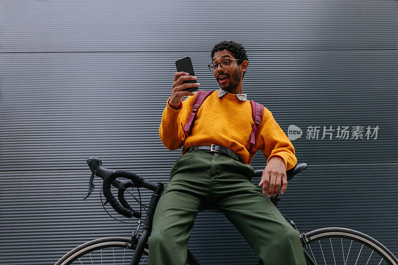 在城市里，年轻人靠在自行车上，使用智能手机
