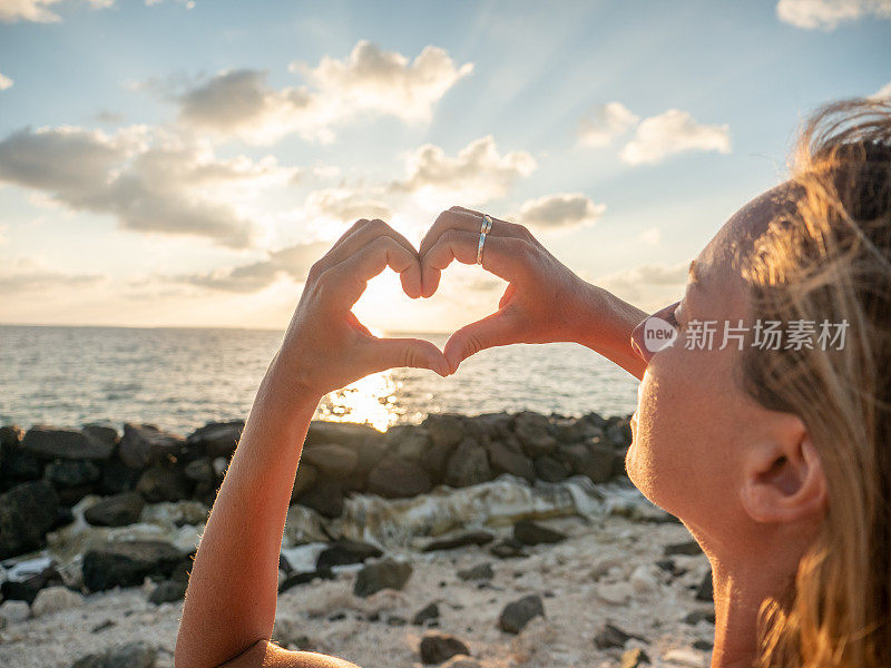 在日出的海滩上，女人用双手制造了一颗心