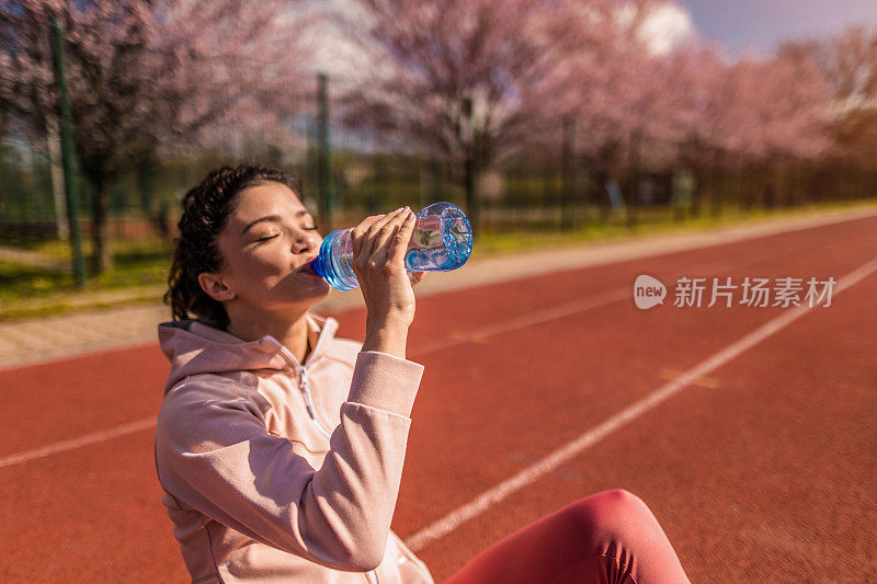 运动的年轻女子在运动轨道上跑步后喝水。