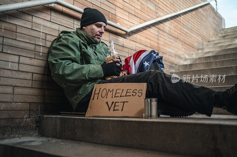 无家可归的老兵拿着美国国旗在街上乞讨，手里拿着一瓶酒