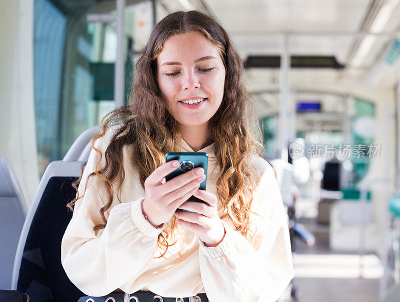 一个积极的女孩在公共交通上的肖像和手机短信