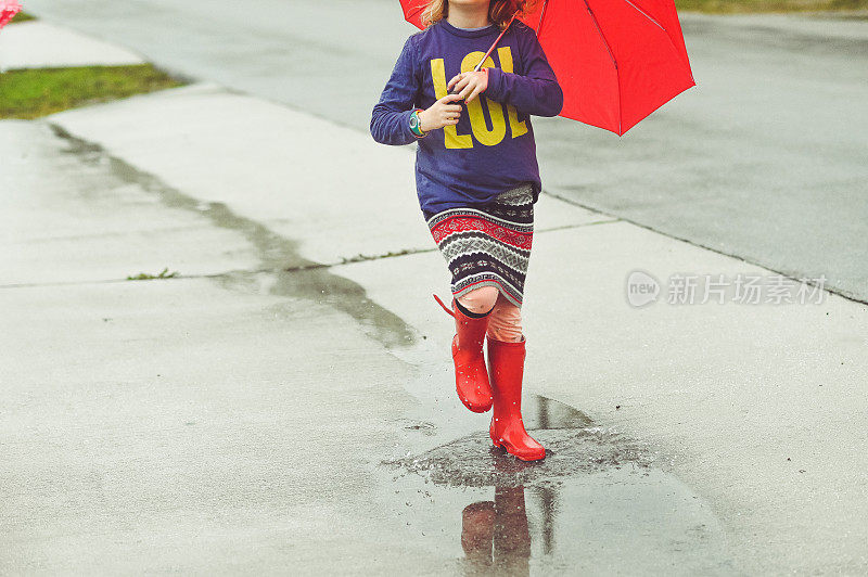 无名的孩子雨靴和伞在雨天的水坑里溅起水花