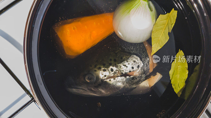 鲑鱼头、洋葱头、胡萝卜头的肉汤在白色煤气炉上的平底锅中煮熟。