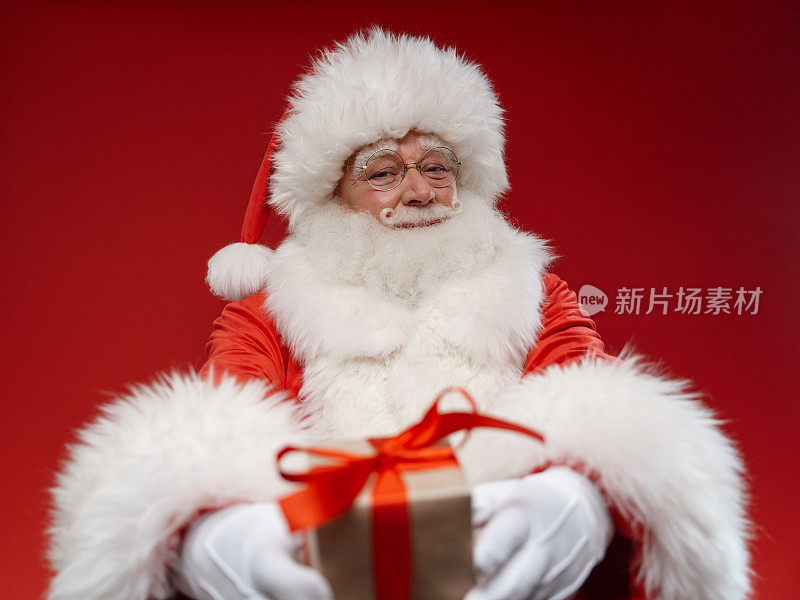 圣诞老人在红色背景下用相机展示礼物的专业照片