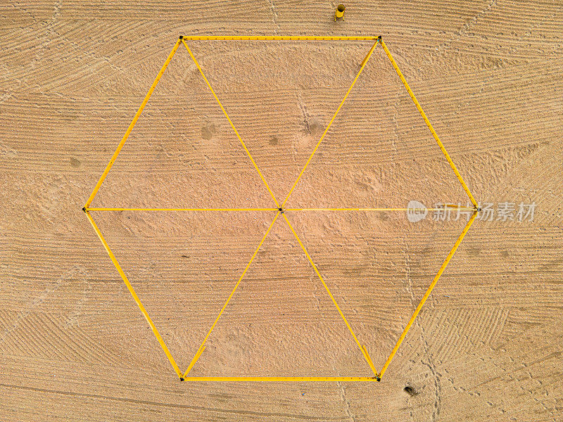 在沙子上用黄色金属制成的六角形框架。俯视图