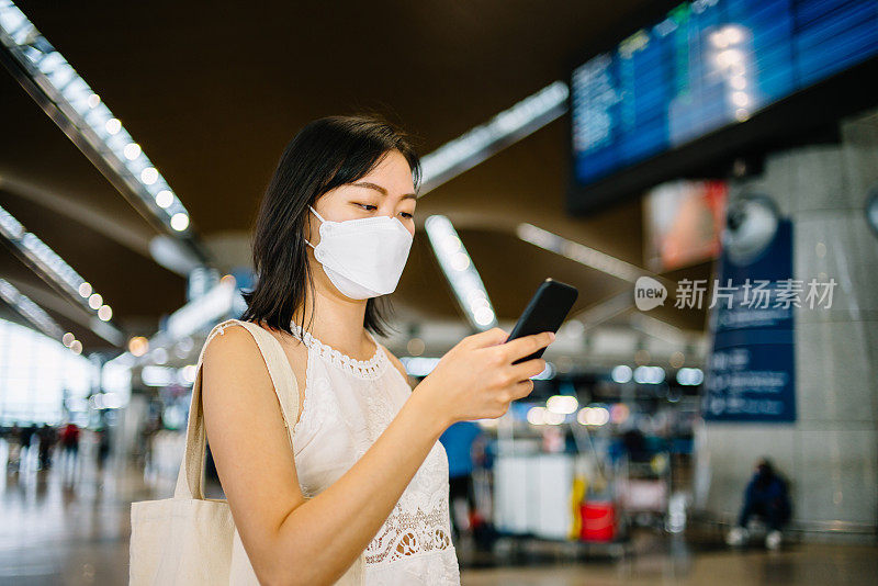 带着防护口罩的亚洲女性游客在机场使用智能手机