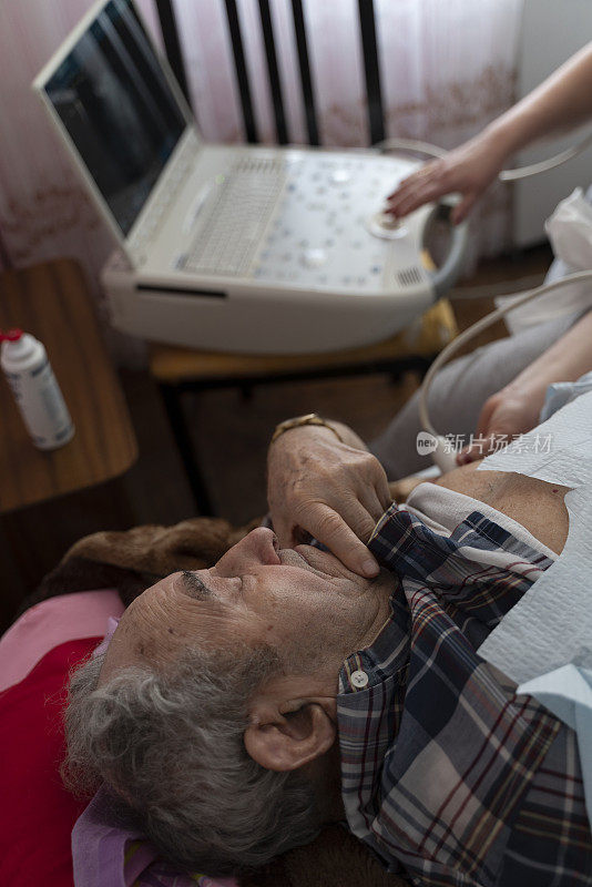 护士——医疗技术人员在家中使用便携式超声波机为97岁的老年男性患者进行超声波心脏健康检查。