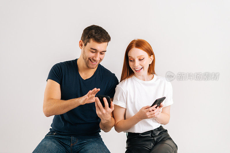 摄影棚拍摄了一对幸福的年轻白人夫妇使用手机，笑着在社交网络上阅读好消息的男人和女人。