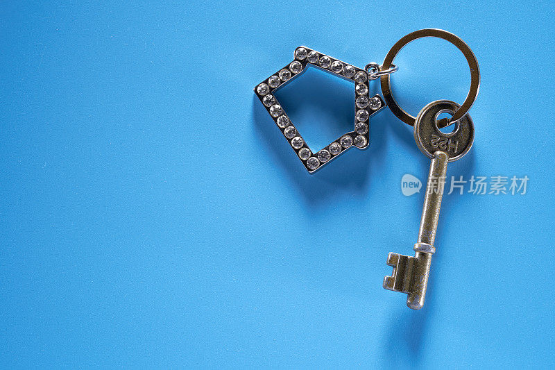 银色的房子形状与钻石钥匙链和钥匙隔离在蓝色