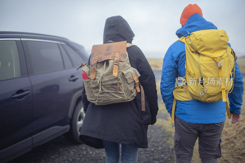 两个背着大背包的徒步旅行者站在汽车旁边。ISL