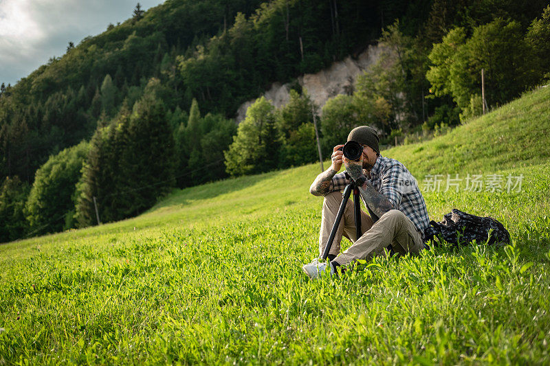 风景摄影师坐在草地上，用无反光镜相机拍摄大自然。
