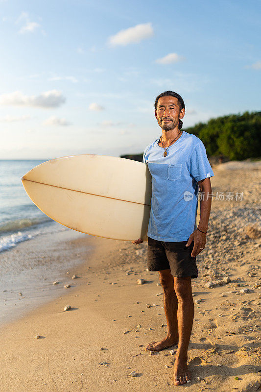 英俊的晒黑的日本冲浪者用冲浪板检查海洋