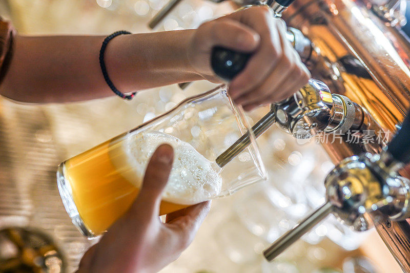 在酒吧或酒吧里，女酒保手拿着啤酒龙头，将桶装啤酒倒进玻璃杯里
