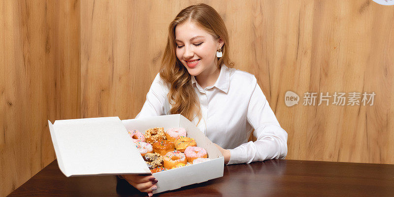 快乐的年轻女子品尝新的甜甜圈和甜甜圈，享受着盒子里的甜食。室内不健康饮食和面包店的概念，人们在咖啡馆或家里拿着和展示甜点