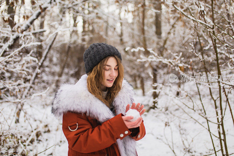 红头发的女人，穿着红外套，皮草，戴着帽子，在冬天的森林里玩雪球。漂亮女人享受假期。女孩在自然界中。感觉幸福。树上的霜和雪。