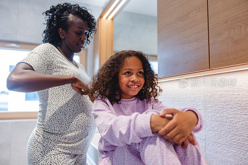 怀孕的黑人母亲早上在一间漂亮的浴室里给女儿梳头