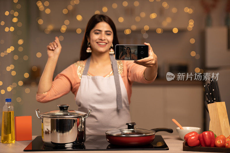 微笑的年轻印度女子在家里厨房做饭时用智能手机自拍的照片