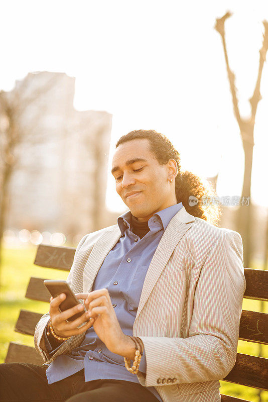 一个快乐的非裔美国人在公园里用智能手机享受周末