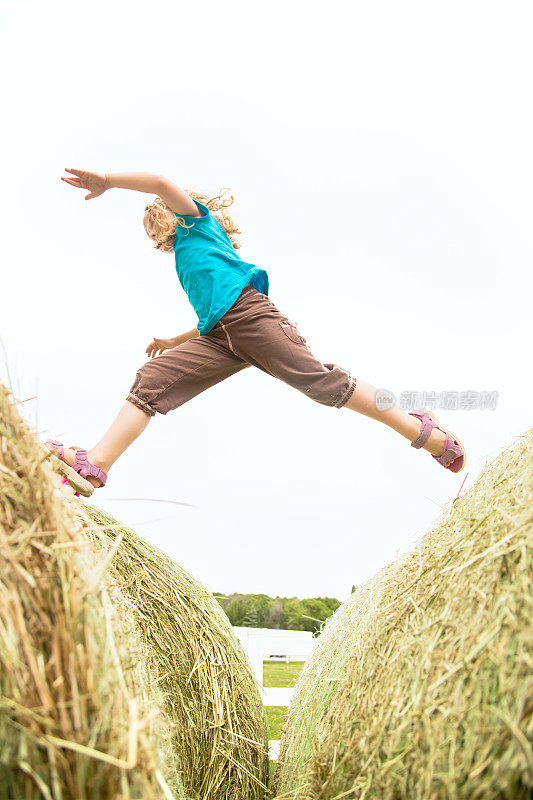年轻的女孩跑和跳过大的圆形干草捆