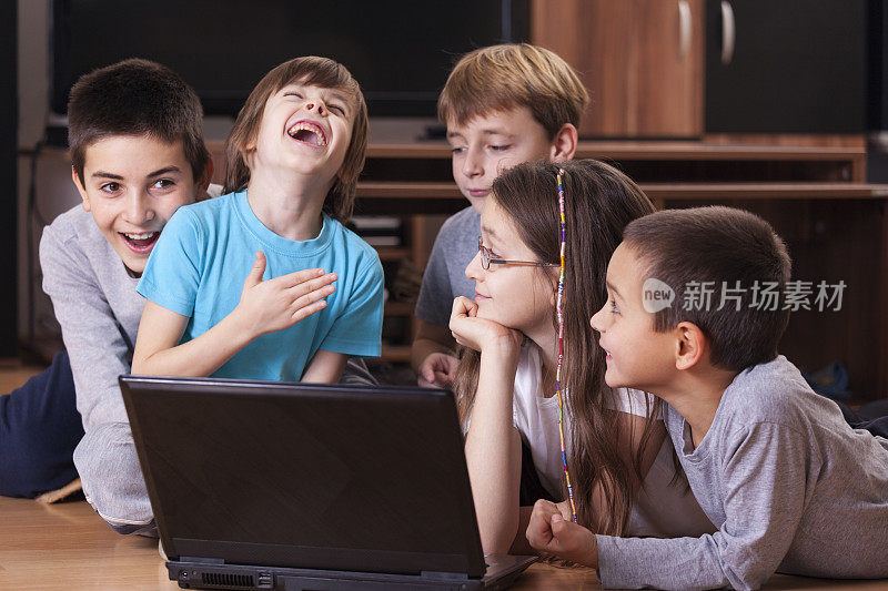 孩子们微笑着躺在地板上，玩着笔记本电脑
